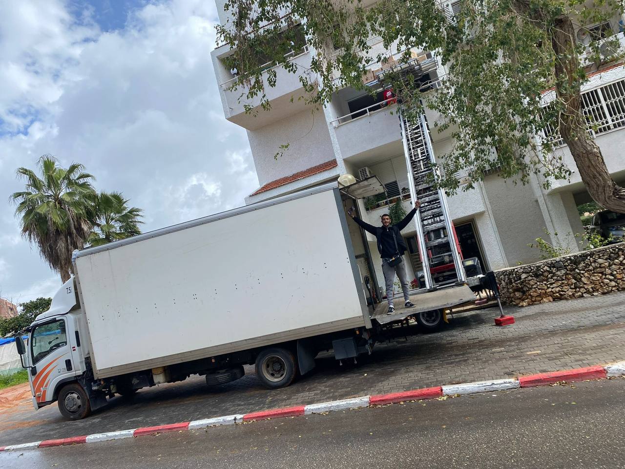 מעלית חיצונית מוצבת מול בניין מגורים, לצד משאית ההובלות של לוי הובלות